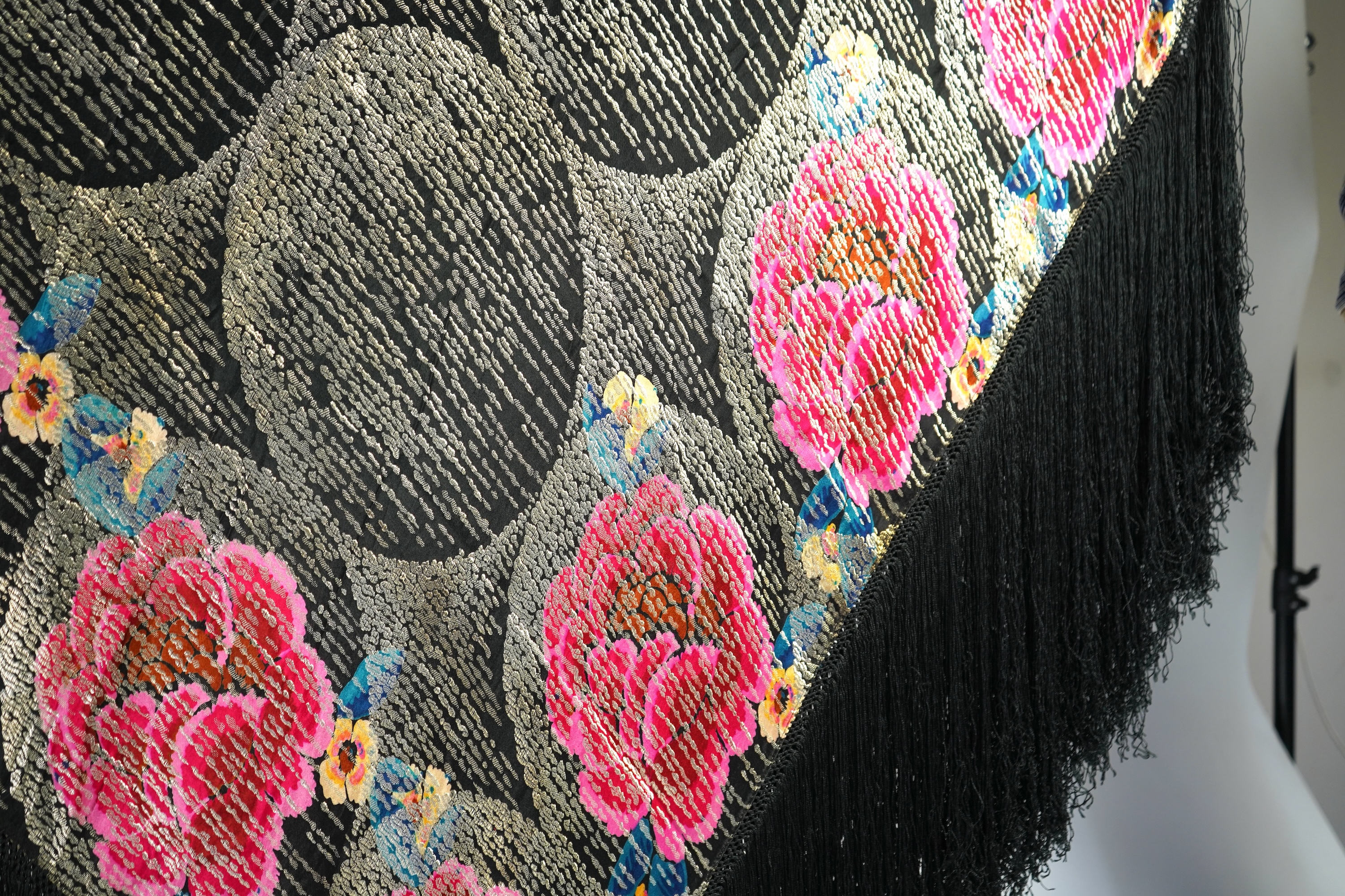 A 1930's ‘jazz age’ black and coloured silk lame evening shawl. Woven with giant pink and red roses and silver thread stripes, edged with long silk fringing. 118cm x 123cm. Condition - colours and silk strong. Fringing g